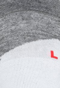 Calcetín gris y blanco con un tejido texturizado. Presenta un patrón curvado distintivo y un pequeño logotipo rojo "L" para la identificación del pie izquierdo.