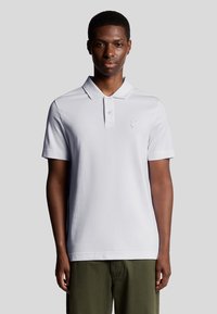 Weißes Poloshirt mit Kragen, kurzen Ärmeln und einem dezenten gestickten Logo auf der Brust. Glattes Baumwollgewebe, taillierte Passform.