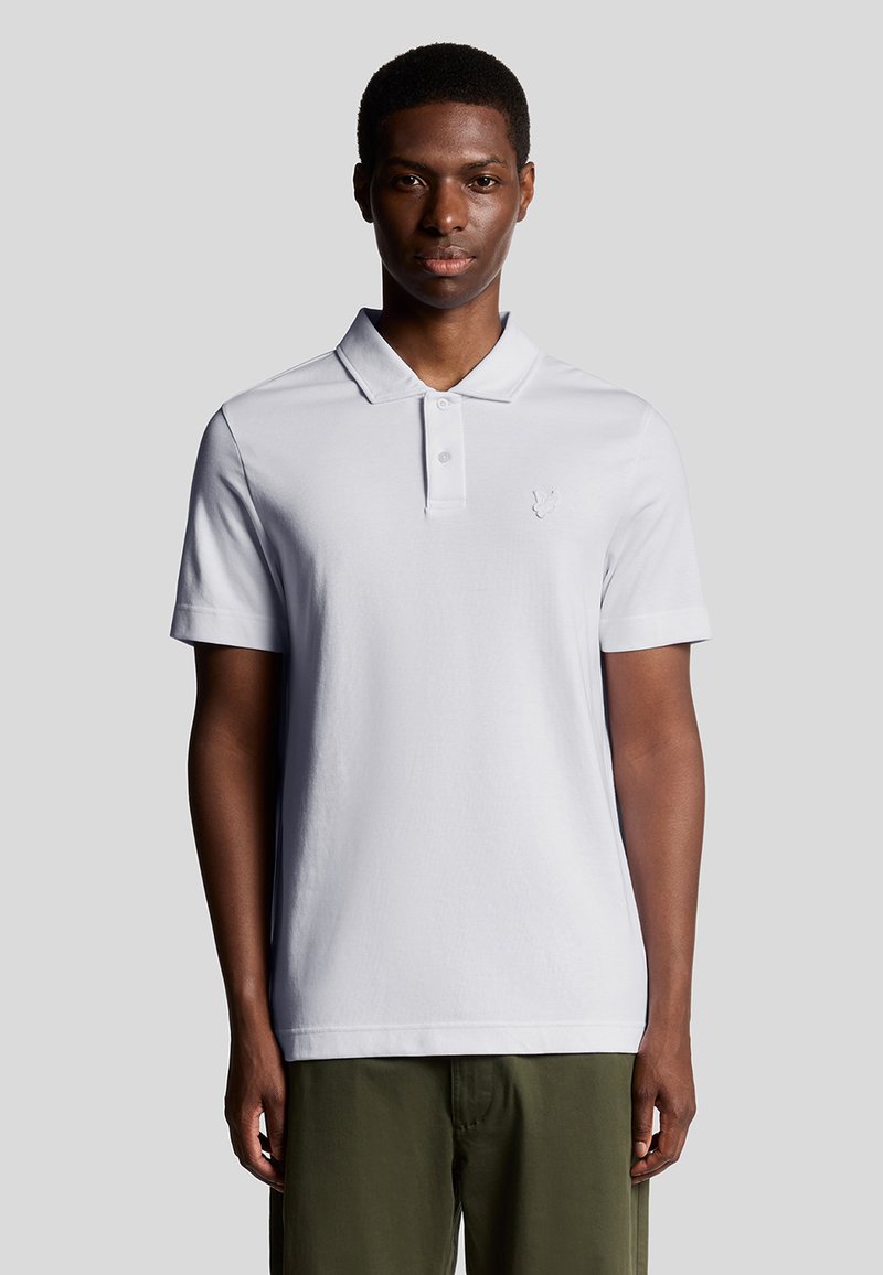 Weißes Poloshirt mit Kragen, kurzen Ärmeln und einem dezenten gestickten Logo auf der Brust. Glattes Baumwollgewebe, taillierte Passform.