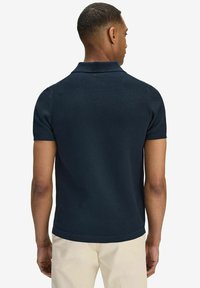 Navy short-sleeve textured polo shirt with a classic collar and ribbed detailing at the hem, worn by a person from the back.