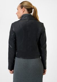 Schwarze Lederjacke mit einem kurz geschnittenen Design, hoher Kragen und glatter Textur, kombiniert mit einem gerippten grauen Rock.