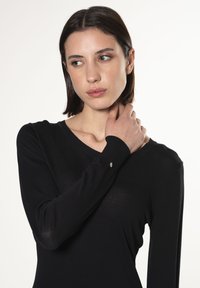 Schwarzes Langarmoberteil mit V-Ausschnitt und einem subtilen Schimmerdetail am Ärmel. Glattes, leichtes Material mit taillierter Passform.