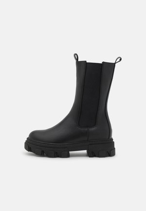 Botte noire en cuir mi-mollet avec semelle épaisse à crampons, panneaux latéraux élastiques et languettes à l'avant et à l'arrière.