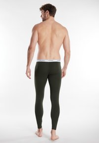 Leggings verde oliva realizzati in tessuto elasticizzato con una vita bianca che mostra il nome del brand, aderenti e con una texture liscia.