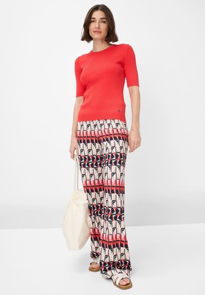 Top corto a righe rosse con maniche corte abbinato a pantaloni larghi con motivo nei colori rosa, rosso e blu navy. Gli accessori includono una borsa color crema e sandali flat.