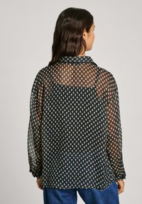 Durchsichtige schwarze Bluse mit einem kleinen geometrischen weißen Muster, Kragen, langen Ärmeln und geknöpften Manschetten. Leicht längerer hinterer Saum.