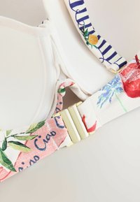 Close-up of bra straps with colorful floral and striped patterns and a gold metal clasp on a light background.