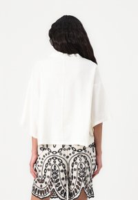 Hvit cropped topp med vide ermer, laget av lett materiale. Kombinert med sort-hvite mønstrede shorts med blomstermotiver.