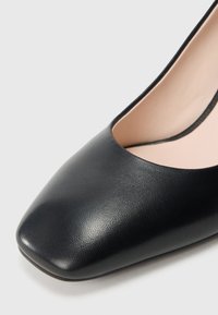 Close-up of the front part of a black leather women's shoe with a square toe and beige interior lining.