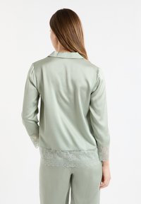 Jasnozielony satynowy top do piżamy z kołnierzykiem i rękawami do łokcia, z koronkowymi akcentami na mankietach i linii dołu.