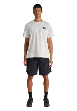 Ung mand iført hvid T-shirt med korte ærmer med "Off Duty Gear" logo, sorte shorts, sorte sokker og sorte sportssko, stående mod hvid baggrund.