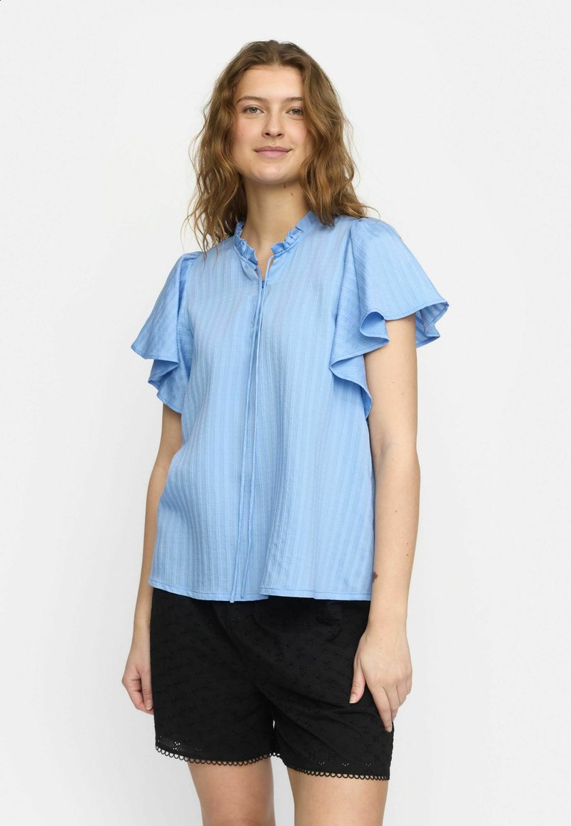 Blusa a righe azzurro chiaro con maniche corte a volant e scollatura rotonda, abbinata a pantaloni corti neri con motivi ad occhio di pernice e rifiniture.