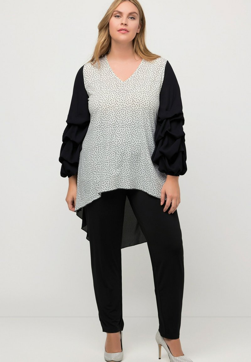 Blusa en blanco y negro con escote en V, un frontal estampado y mangas voluminosas negras. Combinada con pantalones negros y tacones plateados.
