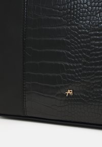 Geantă de mână neagră, realizată din piele netedă și texturată cu un model de crocodil. Accesoriu cu logo auriu pe față. Design elegant și minimalist.