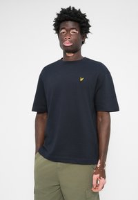 T-shirt en coton noir avec un col rond, des manches courtes et un petit logo d'oiseau jaune sur la poitrine. Design simple, coupe décontractée.