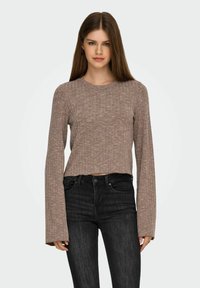 Top corto a maniche lunghe marrone a costine con scollatura rotonda, abbinato a jeans scuri aderenti. La texture appare morbida ed elastica.
