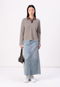 Long-sleeve brown and white striped polo shirt with a brown collar, paired with a light blue denim maxi skirt and white sneakers.