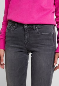 Jeans de mezclilla gris con un diseño clásico de cinco bolsillos, textura ligeramente desgastada y un botón negro en la cintura.