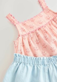 Haut rose à motif floral avec des bretelles festonnées, associé à une jupe bleu clair froncée. Fabriqué en tissu doux, mettant en valeur des détails texturés.