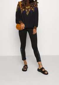 Blusa nera con motivo, a maniche lunghe, caratterizzata da vivaci design geometrici. Abbinata a leggings neri aderenti e sandali neri con fibbie.