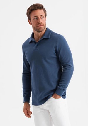 Camisa de polo de manga larga azul, hecha de una tela suave, con cuello plano y puños acanalados, combinada con pantalones blancos.