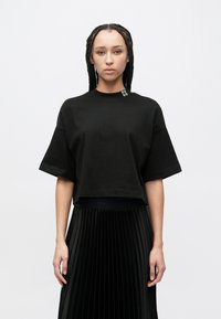 Μαύρο κοντομάνικο κοντό t-shirt από βαμβάκι. Διαθέτει μικρό λογότυπο "HUGO" στη στρογγυλή λαιμόκοψη, συνδυασμένο με μαύρη πλισέ φούστα.