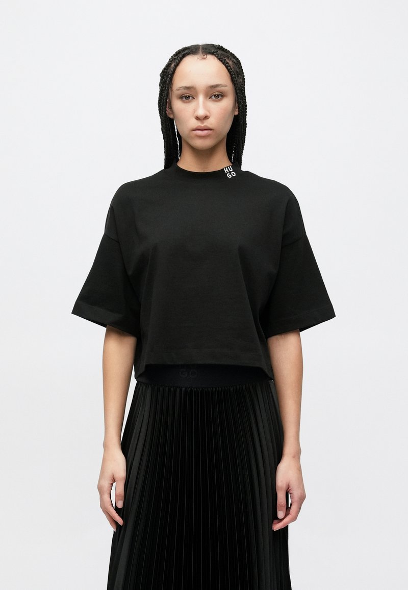 Μαύρο κοντομάνικο κοντό t-shirt από βαμβάκι. Διαθέτει μικρό λογότυπο "HUGO" στη στρογγυλή λαιμόκοψη, συνδυασμένο με μαύρη πλισέ φούστα.