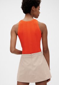 Ribbet orange tanktop med rund halsudskæring, parret med en beige nederdel med lynlås bagpå og en udvidet silhuet.