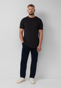 Zwart kortpoloshirt, gecombineerd met donkerblauwe broek en witte sneakers. Eenvoudig ontwerp, gladde textuur en getailleerde vorm.