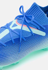 Blue soccer cleat with a textured upper, lightweight design, and a gradient pattern. Features laces and a translucent sole.