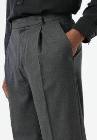 Grijze op maat gemaakte broek met een gladde stoftextuur, voorzien van voorplooien en zijzakken. De tailleband is vlak en wordt gecombineerd met een donker shirt.