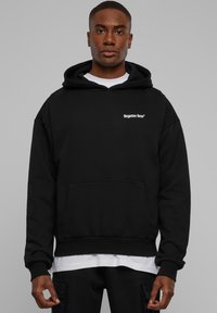 Fekete kapucnis pulóver elülső zsebbel, fehér "forgotten faces" felirat a mellkasnál; puha, texturált anyagból készült.