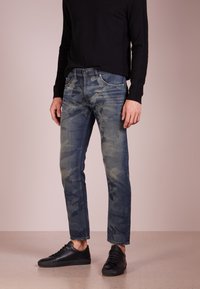 Jeans i denim med ett mönster av mörkblå och ljusblå kamouflage, slim fit, fem fickor och kontrasterande sömmar, kombinerade med svarta sneakers.