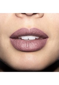 Matowa szminka w odcieniu mauve na pełnych, równych wargach z widocznymi szczegółami tekstury, ukazująca delikatne kontury na tle neutralnej karnacji.