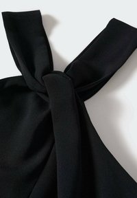Tissu noir noué en un nœud sur fond blanc, montrant une texture lisse et deux larges bretelles s'étendant à partir du nœud.