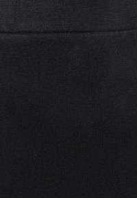 Tissu en tricot noir avec un motif de points serrés et une couture horizontale visible près du bord supérieur.