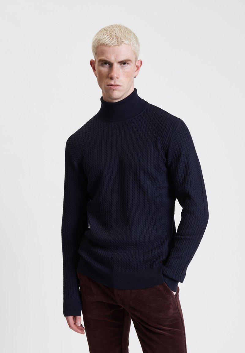 Maglione girocollo in maglia blu navy con un motivo testurizzato, maniche lunghe, polsini a coste e vestibilità rilassata, abbinato a pantaloni marrone scuro.