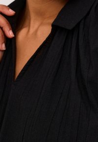 Gros plan sur la main d'une personne touchant le col d'un vêtement noir texturé à col en V avec un col replié.