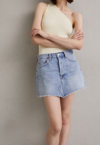 Cremfarbene, gerippte Top mit einem Schulterträger, kombiniert mit einem hellblauen Denim-Minirock mit fransigem Saum und Fünf-Taschen-Design.