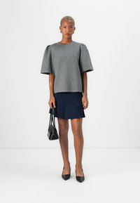 Top grigio a maniche corte con spalle a sbuffo, abbinato a una gonna blu navy. Il modello tiene una piccola borsa nera e indossa scarpe nere con punta affilata.