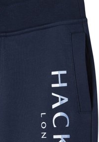 Navy blauwe sweatpants van zachte katoenmix, met een witte "HACK" logo en zijzakken, voorzien van een geribbelde tailleband en een gladde textuur.