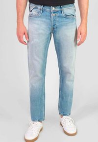 Lichtblauwe denim jeans met een rechte pasvorm, versleten details en een klassiek vijf-pocket ontwerp. Draagt met witte sneakers.