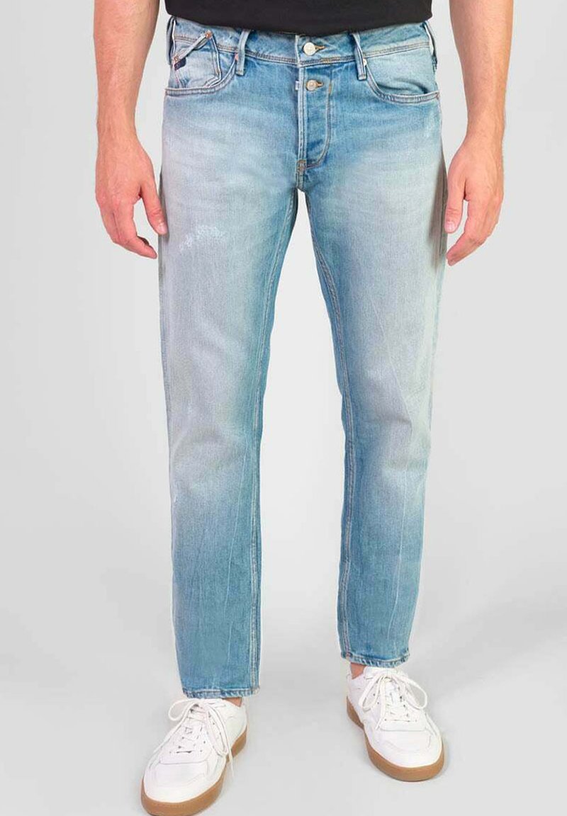 Lichtblauwe denim jeans met een rechte pasvorm, versleten details en een klassiek vijf-pocket ontwerp. Draagt met witte sneakers.