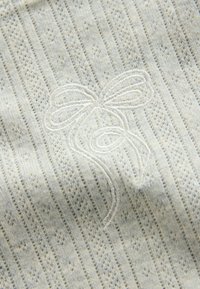 Valge kootud kangas vertikaalsete pitsiribadega, millel on valgest niidist tikitud lipsu ja lillemuster.