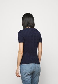 Navy blue knitted short-sleeve sweater with a textured cable pattern, fitted shape, and ribbed hem, paired with light blue denim jeans.