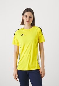 Geltonas sportinis marškinėliai trumpomis rankovėmis, su juodais pečių juostelėmis ir baltais šonais. Pagaminti iš lengvos medžiagos; turi Adidas logotipą.