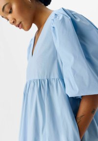 Robe bleu clair en coton, dotée d'un décolleté en V profond, de manches à volants et d'une taille froncée, créant une silhouette ample et fluide.