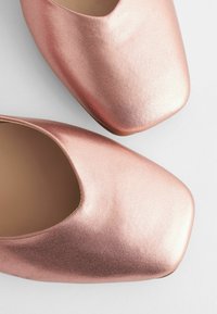 Zapatos de oro rosado de punta abierta con un acabado metálico elegante, diseño de punta cuadrada y textura suave. Presentan un brillo sutil y un interior suave.
