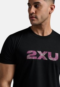 Svart t-shirt av mjukt tyg med en stor, slitna rosa "2xu" logotyp på framsidan. Korta ärmar med rundad nackdesign.
