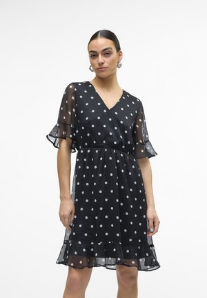 Abito nero a pois con maniche corte e volants, scollatura a V e vita aderente. Realizzato in tessuto leggero e trasparente con orlo svasato.